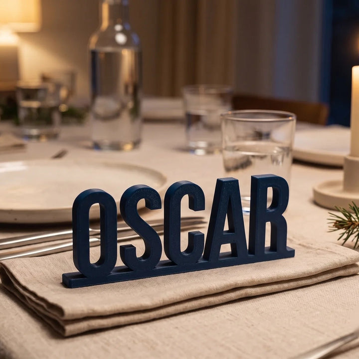 Marcasitios personalizado con el nombre Oscar en letras exentas sobre base, en azul noche junto a un plato de mesa