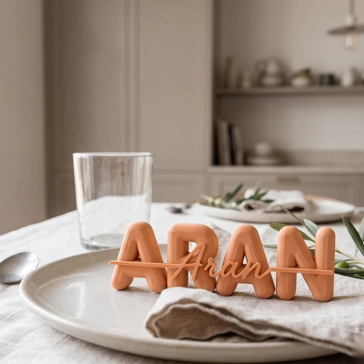 Marcasitios personalizado con el nombre Aran en mayúsculas y caligrafía superpuesta, en tono caramelo sobre un plato de mesa