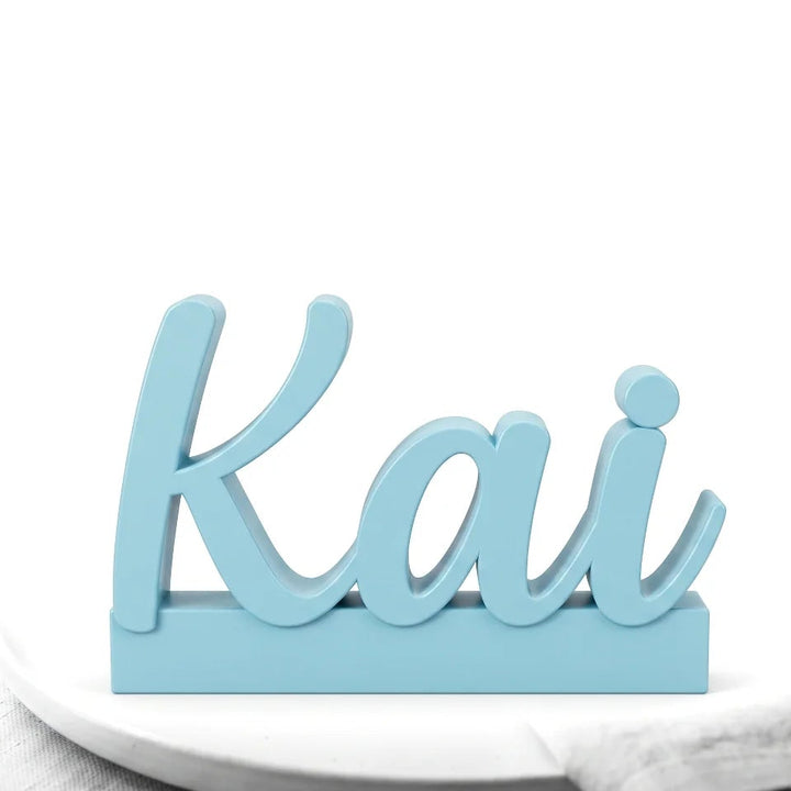 Marcasitios con el nombre Kai en caligrafía sobre base, en azul celeste apoyado en un plato