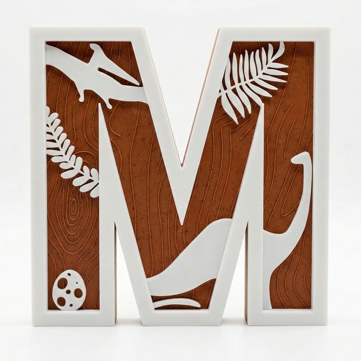 Primer plano de letra M decorativa con siluetas de dinosaurios y hojas en color blanco sobre fondo texturizado marrón terracota.