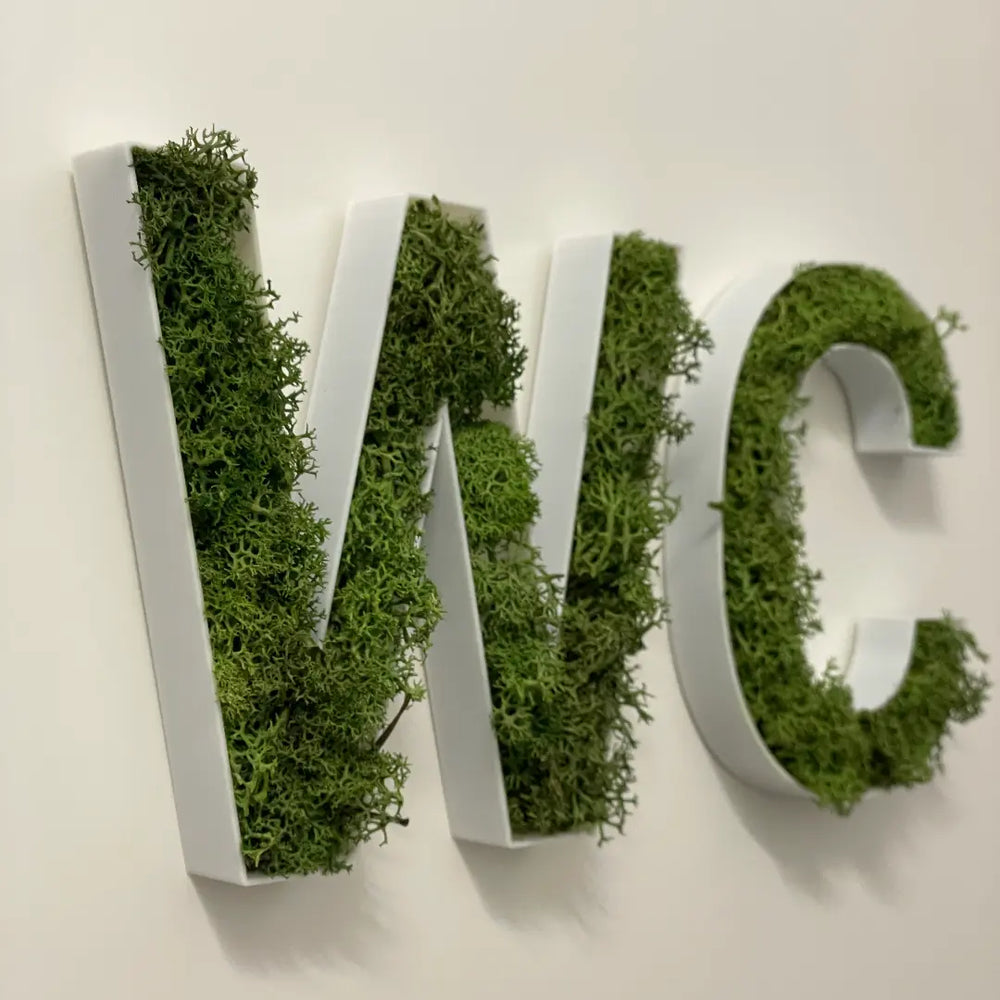 Letras rellenas de musgo verde montadas en pared, ejemplo de uso vertical decorativo.