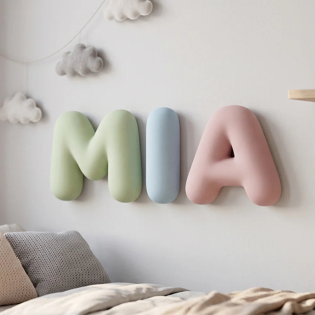 Name in dekorativen Bubble-Buchstaben in Salbeigrün, Himmelblau und Puderrosa an einer weißen Wand