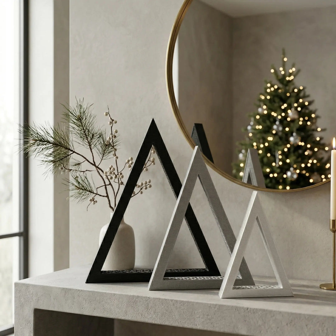 Composición de tres árboles navideños minimalistas en forma de triángulo negro, gris y blanco en consola moderna.