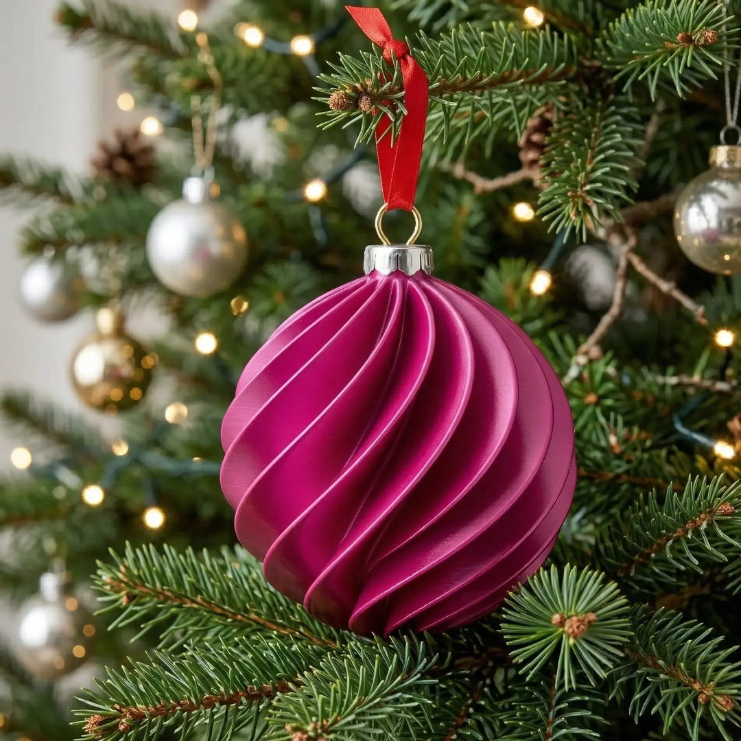 Bola de Navidad ornamental con diseño helicoidal en color magenta mate colgada con cinta roja en un árbol iluminado.