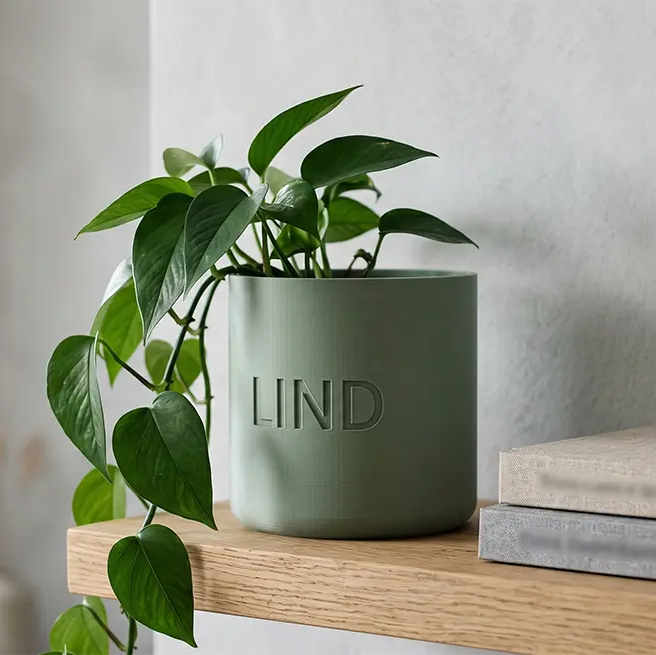 Sage green Nordic planter with engraved name Lind next to a round mirror on a stone shelf