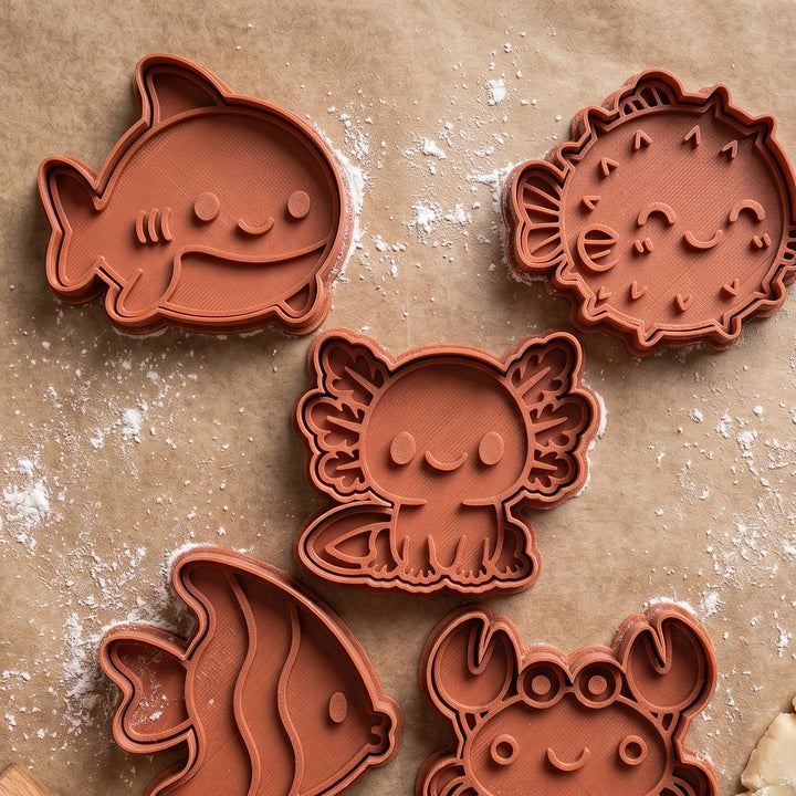 Conjunto de cinco cortadores de bolachas em forma de animais do mar em cor terracota sobre papel vegetal.