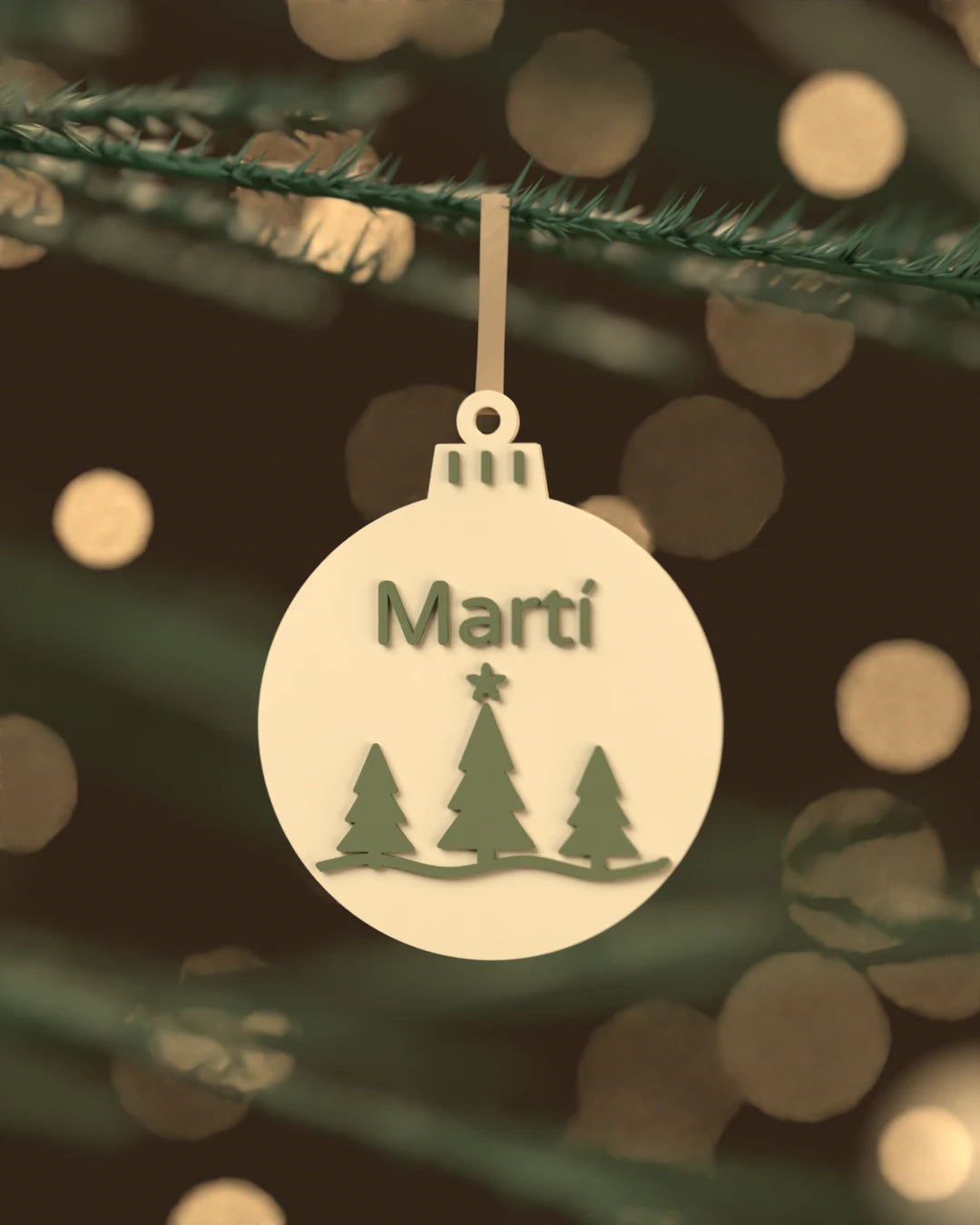Bola de Navidad Abeto color blanco hueso con abetos y el nombre Martí en verde oscuro, colgada de una rama de abeto