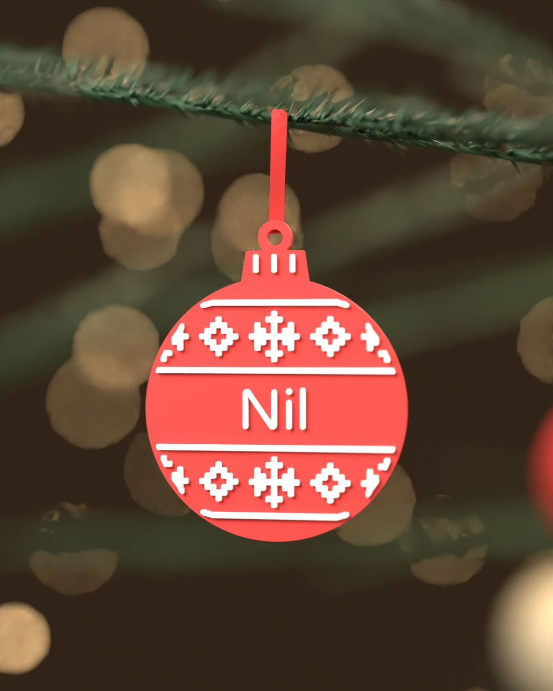 Bola de Navidad Nórdica roja con patrón de jersey y el nombre Nil en blanco, colgada de una rama de abeto