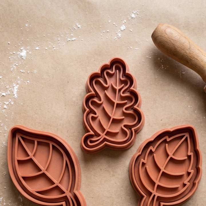 Conjunto de três cortadores de bolachas em forma de folhas em cor terracota sobre papel vegetal.