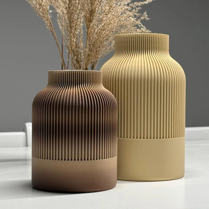 Jarrón tono terracota degradado con espigas secas junto a jarrón amarillo mostaza en ambiente cálido.