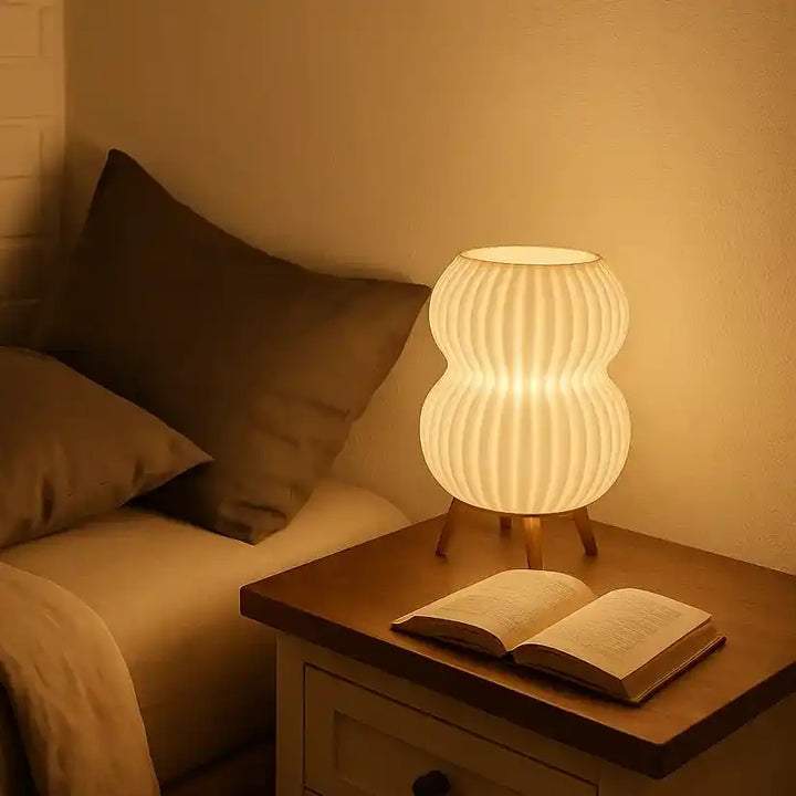 Lámpara de mesita de noche cilíndrica color beige en bioplástico PLA con bombilla encendida.