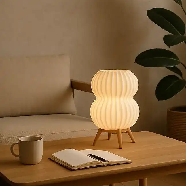 Lámpara de mesa cilíndrica color beige en bioplástico PLA con bombilla encendida.