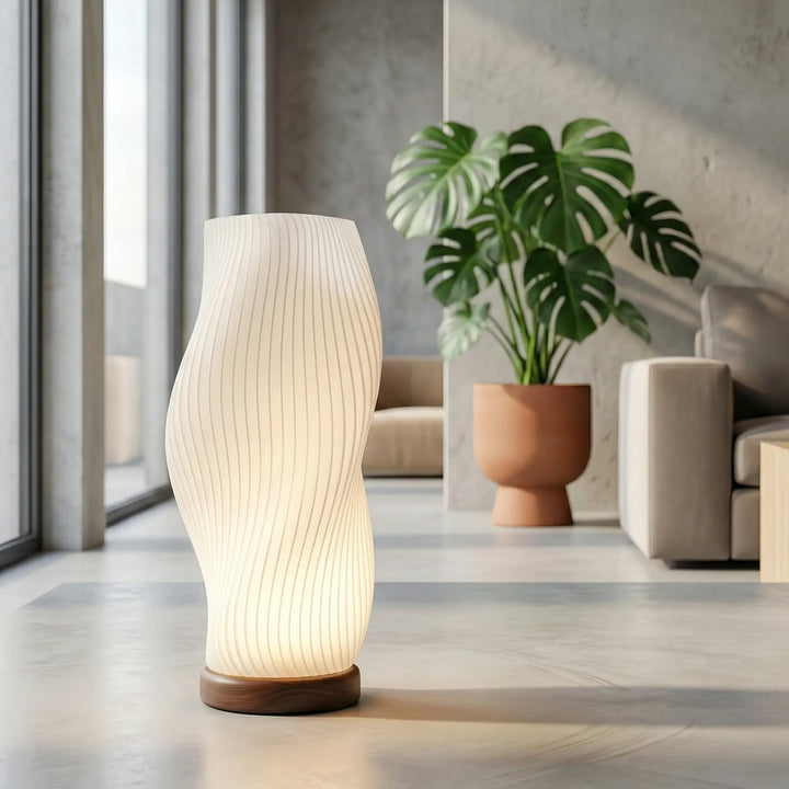 Lámpara de mesa moderna con forma ondulada y textura acanalada blanca, encendida con luz cálida y base redonda.