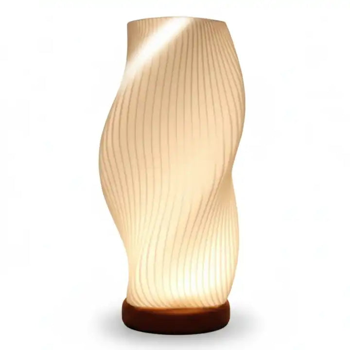 Lámpara de mesa moderna con forma ondulada y textura acanalada blanca, encendida con luz cálida y base redonda.