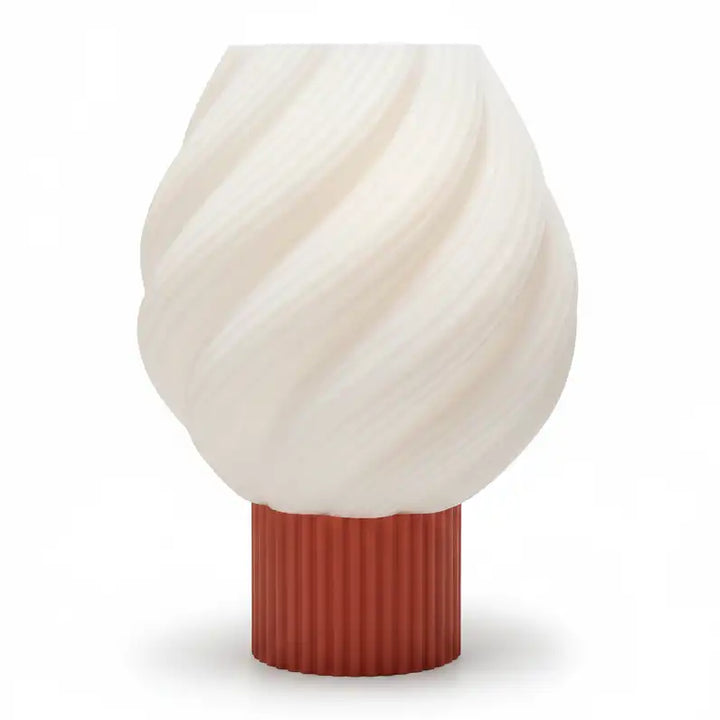 Lámpara de mesa moderna con pantalla blanca en espiral y base cilíndrica azul personalizable en color texturizada sobre superficie blanca.