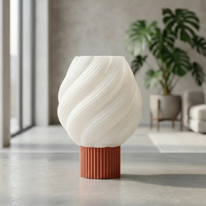 Lámpara de mesa moderna con pantalla blanca en espiral y base cilíndrica azul texturizada sobre superficie blanca.