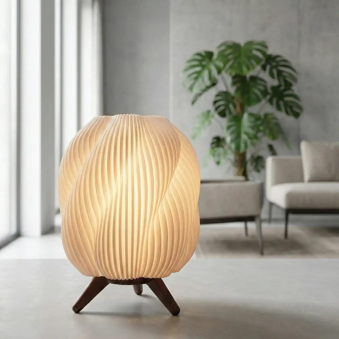 Lámpara de mesa con diseño en espiral blanca iluminada con luz cálida sobre superficie oscura, estilo minimalista moderno.