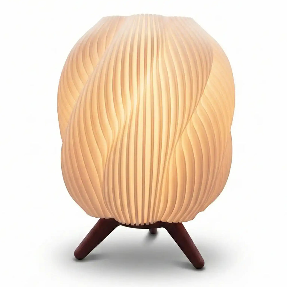 Lámpara de mesa con diseño en espiral blanca iluminada con luz cálida sobre superficie oscura, estilo minimalista moderno.