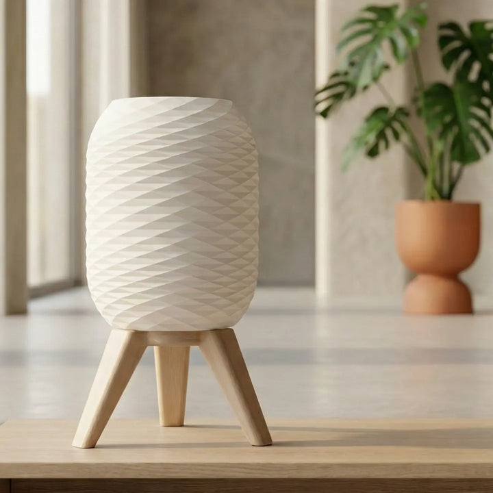 Lámpara de mesa moderna con pantalla blanca de textura diamante y patas trípode efecto madera clara encendida sobre superficie lisa.