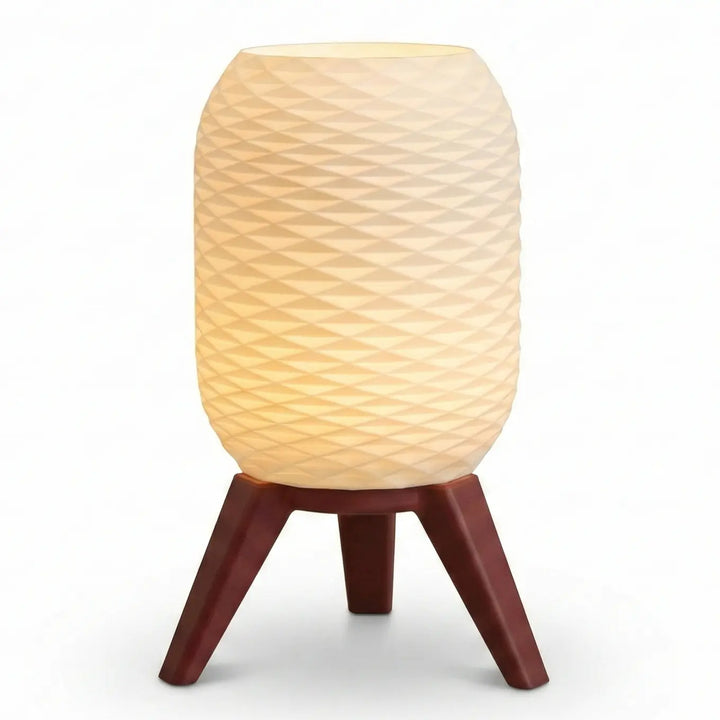 Lámpara de mesa moderna con pantalla blanca de textura diamante y patas trípode efecto madera clara encendida sobre superficie lisa.