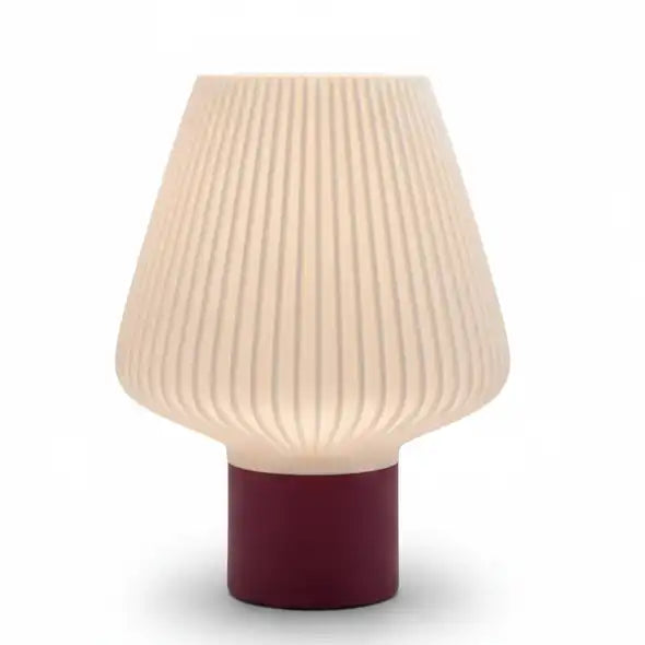 Lámpara de mesa moderna con pantalla blanca facetada y cable textil gris encendida sobre mesita de noche.