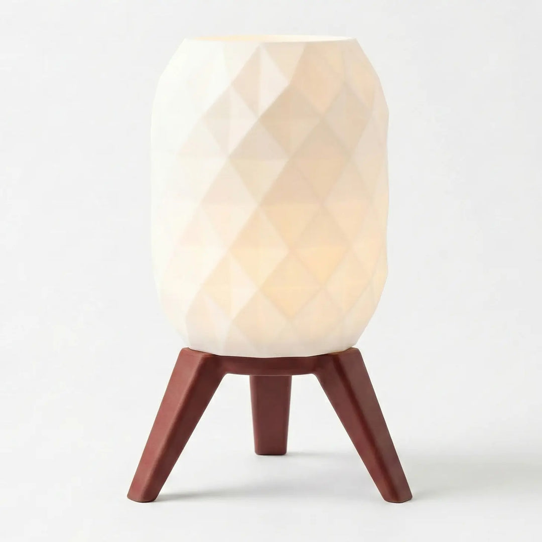 Eingeschaltete Tischlampe mit weißem geometrischem Schirm und Beinen in heller Holzoptik auf einem grauen Tisch.