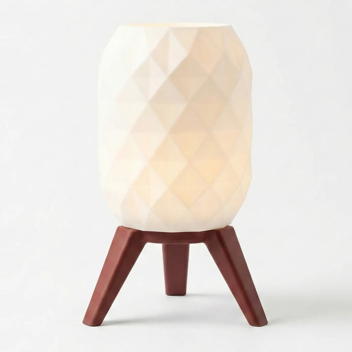 Eingeschaltete Tischlampe mit weißem geometrischem Schirm und Beinen in heller Holzoptik auf einem grauen Tisch.