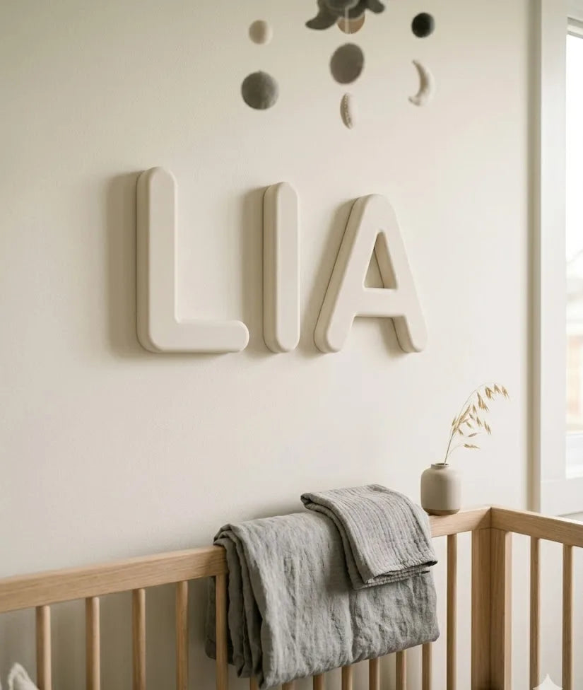 Letras decorativas personalizadas con el nombre LIA en blanco hueso, tipografía redondeada nórdica, sobre pared de habitación infantil
