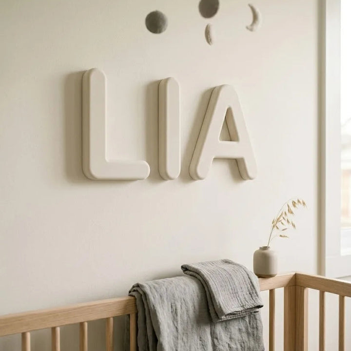 Letras decorativas personalizadas con el nombre LIA en blanco hueso, tipografía redondeada nórdica, sobre pared de habitación infantil