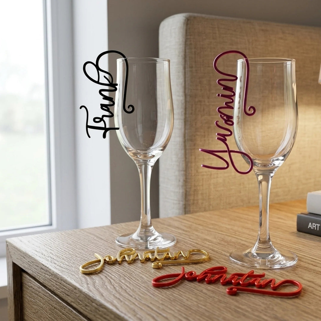 Marcasitios de copa personalizados con nombres en caligrafía script en negro, lila, dorado y rojo colgados sobre copas de vino