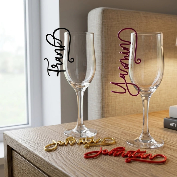 Marcasitios de copa personalizados con nombres en caligrafía script en negro, lila, dorado y rojo colgados sobre copas de vino