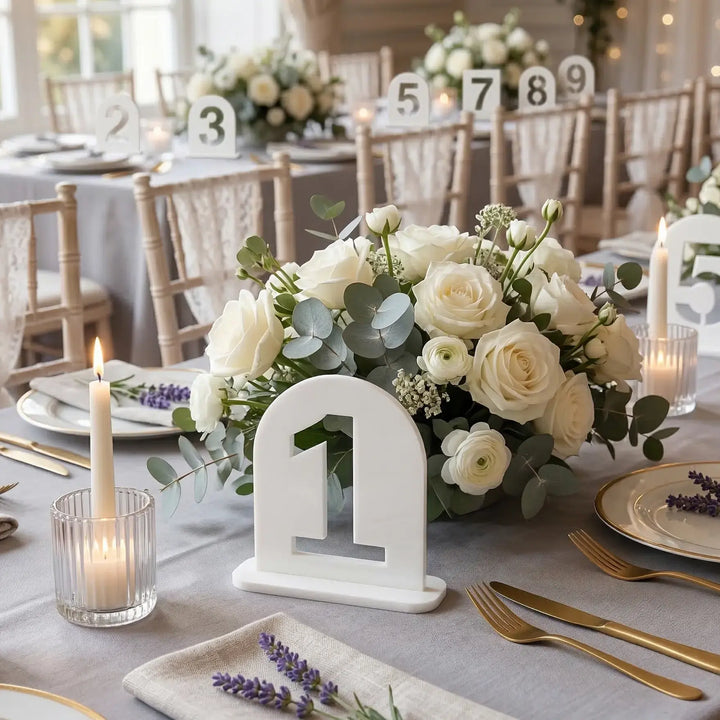 Numéro de table en arche blanche avec chiffre un ajouré sur une table de mariage avec fleurs blanches et bougies.
