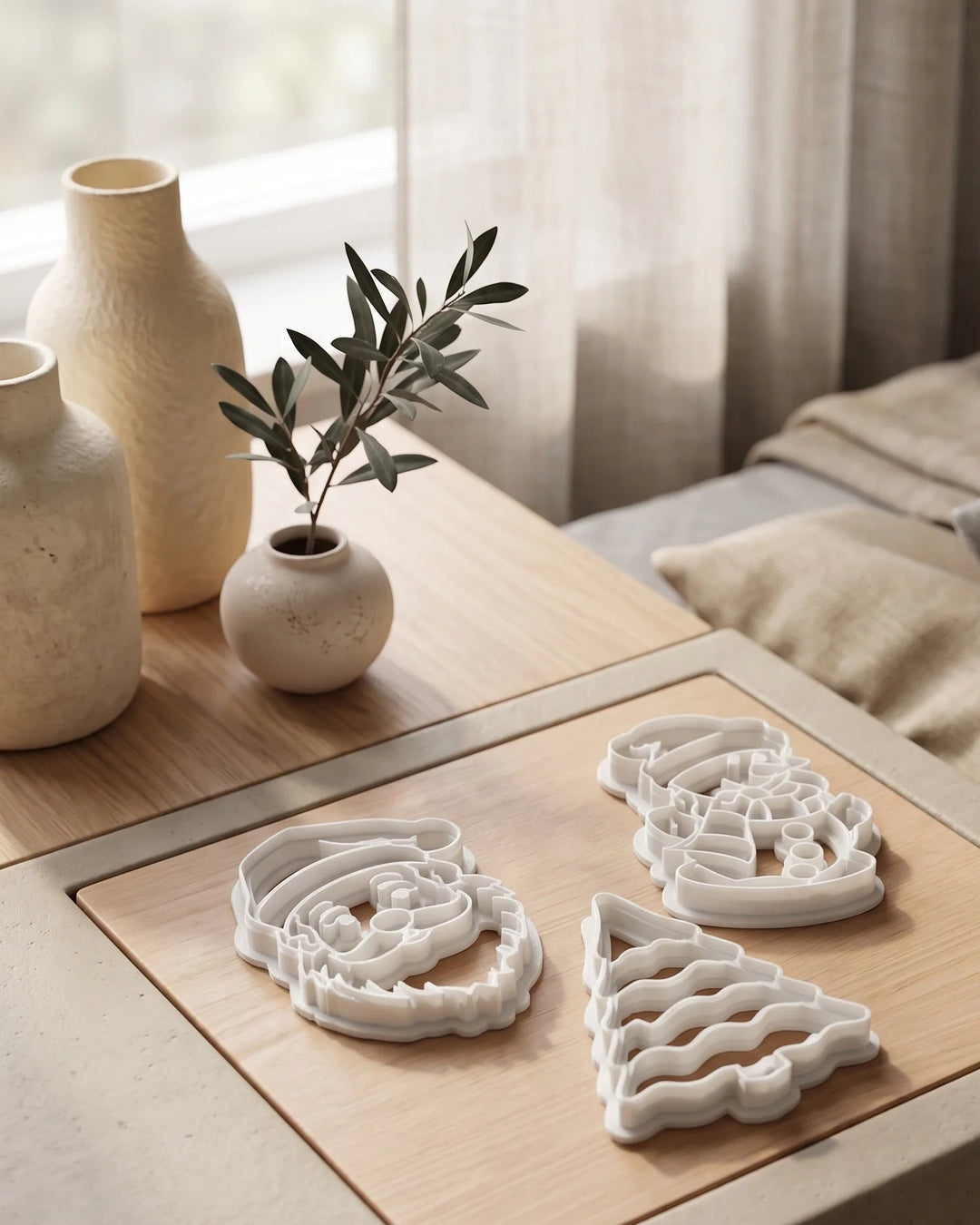 Set of three white cookie cutters shaped like Santa Claus, a Christmas tree and a snowman on a wooden table.
