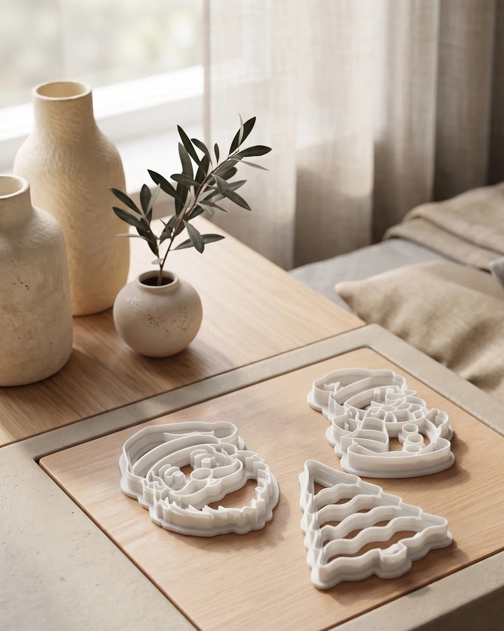 Set of three white cookie cutters shaped like Santa Claus, a Christmas tree and a snowman on a wooden table.